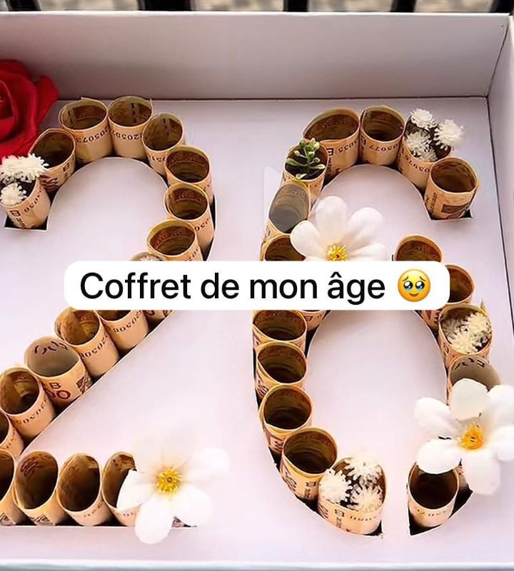 Coffret avec des billets roulés formant un nombre et des fleurs blanches